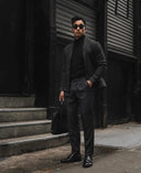 Man in cashmere office wear, black turtleneck, charcoal jacket and trousers, standing outdoors, full front view