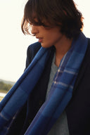 Model showing how to wear a cashmere scarf draped over a navy blazer, blue checked pattern, side view