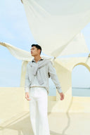 Man outdoors in gray shirt and white pants with knit cashmere travel essentials draped over shoulders