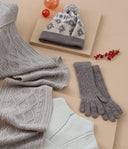 Flat lay of cashmere gifts for holidays: cable knit blanket, patterned pom hat, gray gloves and white sweater