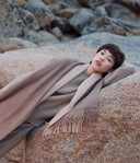 Model resting on rocks wearing fringed striped scarf and coat, showing Mongolian cashmere craftsmanship