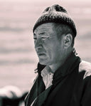 Mongolian herder in a knit hat and collared jacket, black and white close-up portrait outdoors