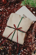 Folded cream cashmere Christmas sweater tied with red and green ribbons on festive tinsel, flat lay