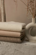 Folded beige cashmere sweaters stacked with white and taupe knits beside a pale ceramic vase, flat lay