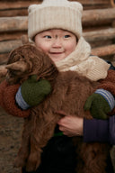 Child in cream knit hat and scarf holding a brown cashmere goat kid, showing cashmere origin traceability