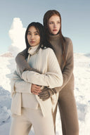 Two models in snow wearing the undyed cashmere collection in natural white and brown shades, cable scarf and gloves