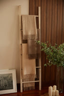 Fringed cashmere blankets draped on a wooden ladder beside candles, eucalyptus and a framed goat photo