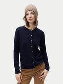 Woman wearing a navy cardigan, beige beanie, and brown pants on a light gray background  #color_taupe