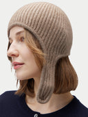 Person wearing a beige knitted hat with ear flaps on a white background. #color_taupe