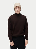 front view of a man wearing a beige beanie with brown sweater and black pants