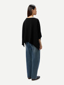 Back view of a person wearing a black poncho and blue jeans on a white background #color_black