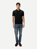 Man wearing a black polo shirt and blue jeans on a white background
