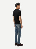 Man wearing a black polo shirt and blue jeans on a white background