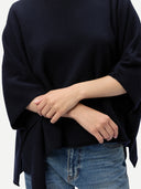 a zoomed-in shot of a person wearing a dark navy poncho and blue jeans with hands clasped in front on a white background #color_navy-blazer