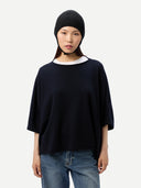 close up front view of a woman wearing a black knitted aviator cap, navy poncho  and blue jeans on a light gray background #color_black