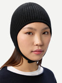 close up side view of a woman wearing a black knitted aviator cap, navy poncho  on a light gray background #color_black