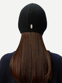 close up beck view of a woman wearing a black knitted aviator cap with a small brand label "GOBI", navy poncho   on a light gray background #color_black