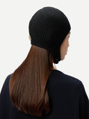 close up back view of a woman wearing a dark gray knitted aviator cap with a small label "GOBI", navy poncho on a light gray background #color_black