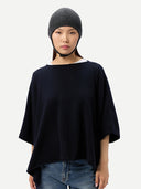 close up front view of a woman wearing a dark gray knitted aviator cap, navy poncho  and blue jeans on a light gray background #color_charcoal