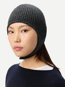 close up side view of a woman wearing a dark gray knitted aviator cap, navy poncho  on a light gray background #color_charcoal