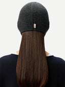 close up back view of a woman wearing a dark gray knitted aviator cap with a small brand label "GOBI", navy poncho   on a light gray background #color_charcoal