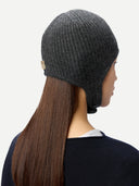 close up back view of a woman wearing a dark gray knitted aviator cap with a small label "GOBI", navy poncho on a light gray background #color_charcoal