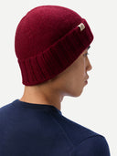 back view of a man wearing a dark red beanie and navy top in a light gray background.