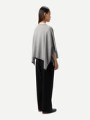 back view of a woman wearing a gray poncho and black pants on a white background #color_high-rise