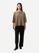 Woman wearing a brown poncho and black pants on a white background