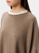 Close-up of a person wearing a soft taupe knit sweater over a white crew-neck undershirt, against a plain light background.