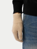 Beige glove worn by a person with a black sleeve and blue jeans on a light gray background #color_beige