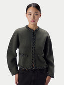 A model wearing a dark olive green cropped knit jacket with braided trim details, paired with black jeans, against a light gray studio background.