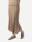 Side-bottom view of person wearing a beige ribbed sweater and skirt set with gray shoes on a white background #color_warm-grey