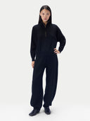 A model stands against a light gray studio background wearing a matching black knit loungewear set consisting of a half-zip long-sleeve top and wide-leg pants.