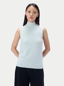 A model wearing a light icy blue sleeveless mock neck knit sweater vest paired with dark navy pants, set against a solid light gray background.
