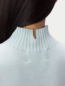 Close-up back view of a person wearing a pale icy blue ribbed knit sweater with a small keyhole cutout at the back of the neck.
