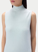A close-up of a model wearing a pale icy blue ribbed knit sleeveless mock neck top against a light gray background.