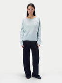 A model stands against a light gray studio background wearing a pale icy blue long-sleeve knit top and dark navy wide-leg trousers.