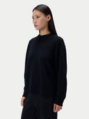 A woman modeling a black long-sleeve knit sweater against a plain light gray studio background.