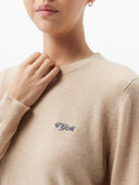 Close-up of a woman wearing a beige cashmere crewneck sweater with embroidered initials on the chest.  #color_jade-lime