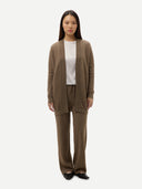 A model stands against a light gray studio background wearing a matching taupe knit cardigan and wide-leg pants set over a white top and black flats.