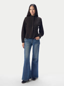 A woman modeling a dark brown button-front knit cardigan with a mock neck, paired with blue flare jeans and black shoes, against a plain light gray studio background.