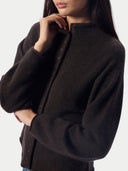 A close-up of a model wearing a dark brown, long-sleeved knit cardigan with a buttoned stand collar.