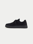 A side profile view of a low-top sneaker featuring a black-colored knit upper and matching laces. The shoe has a smooth suede-like heel counter and eyelet overlays in the same tone, in a white background. #color_black