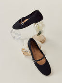 A pair of black mercerized wool cashmere knitted ballet flats with a leather strap buckle closure, displayed on a wooden surface with a decorative background. #color_black