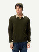 Man wearing a green sweater over a beige shirt with blue jeans on a white background #color_avocado
