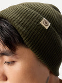 close up of a man wearing an olive green beanie with a logo on a white background #color_avocado