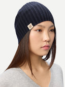Woman wearing a navy blue beanie with a brand logo on a light gray background  #color_navy-blazer