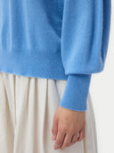 Close-up of a blue dolman sleeve, ribbed cuff sweater and white pants on a plain background #color_azure-blue