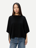 Woman wearing a black poncho and blue jeans on a white background #color_black
